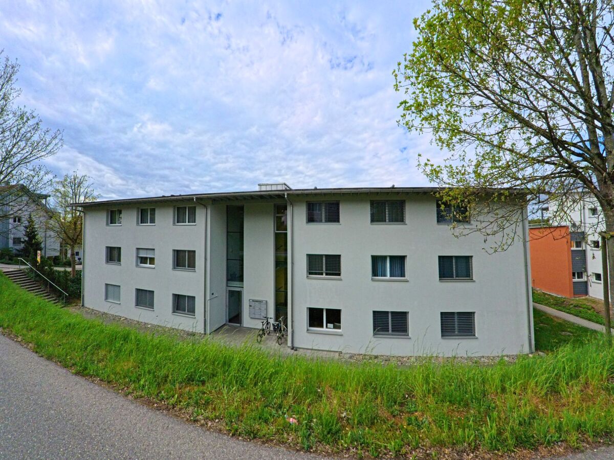 Ein modernes Mehrfamilienhaus mit schlichter Fassade befindet sich in Dachsen im PLZ-Bereich 8447 im Kanton Zürich am Rand eines Wohnquartiers.