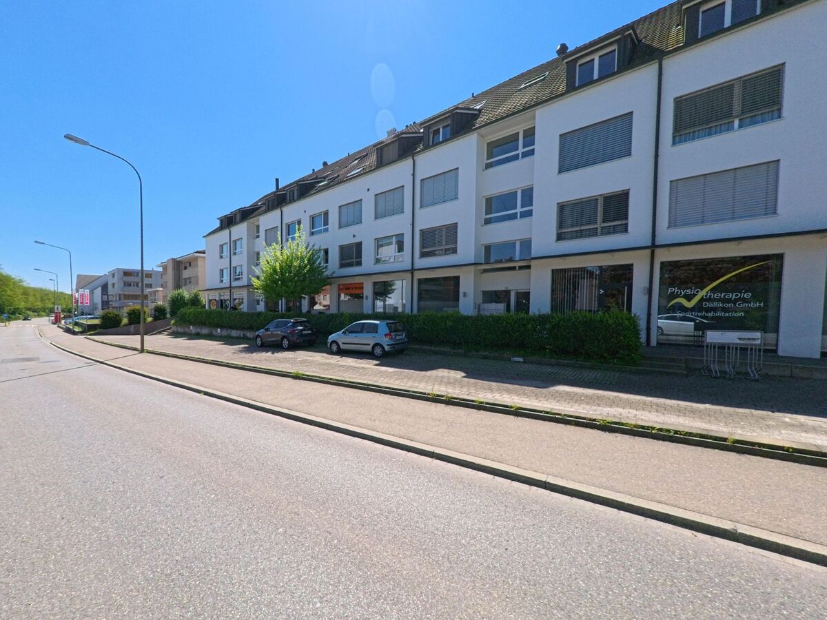 Ein Geschäfts- und Wohnhaus mit einer Physiotherapiepraxis befindet sich in Dällikon im PLZ-Bereich 8108 im Kanton Zürich an einer breiten Hauptstrasse mit Parkplätzen.