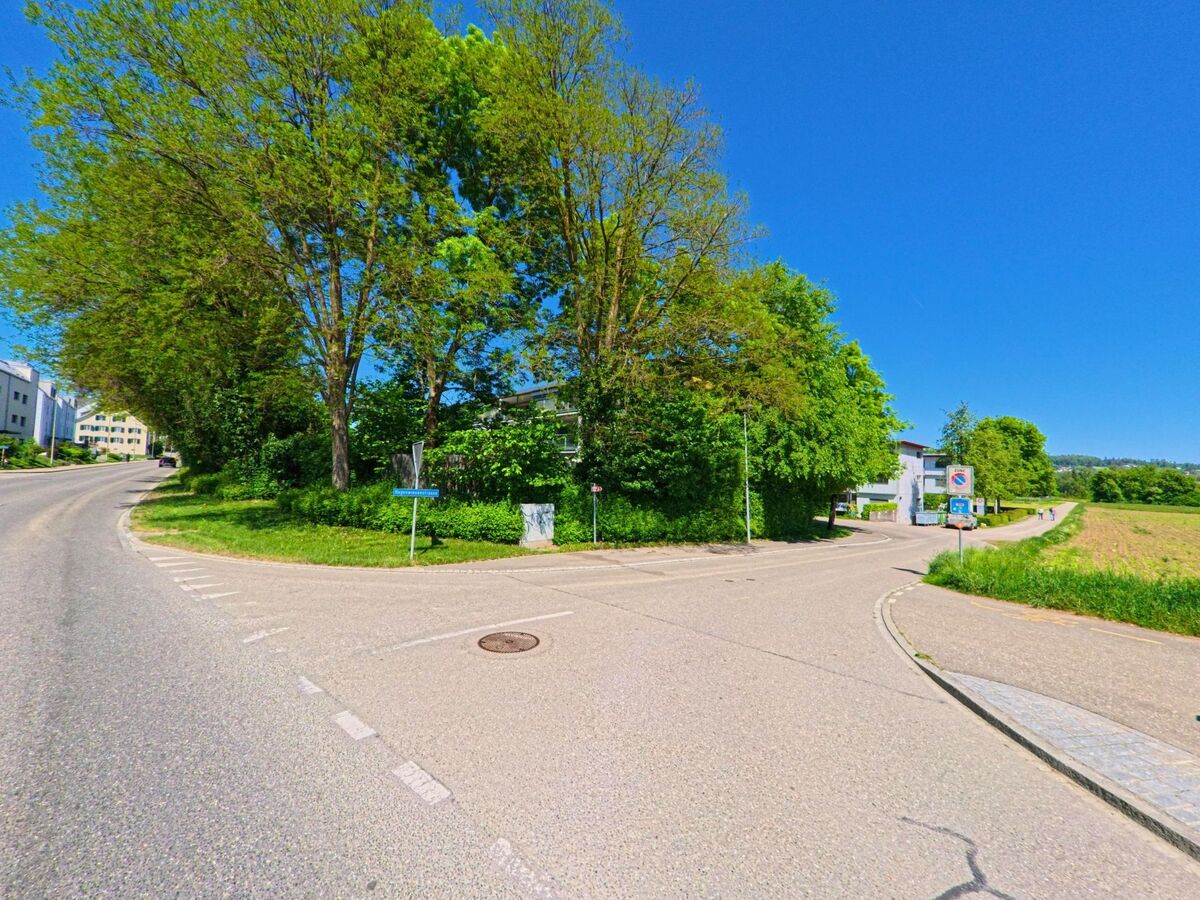 In Dällikon im Kanton Zürich mit der Postleitzahl 8108 zweigt ein Weg von der Hauptstrasse ab und führt entlang eines Feldrandes in ein Wohngebiet mit Bäumen.