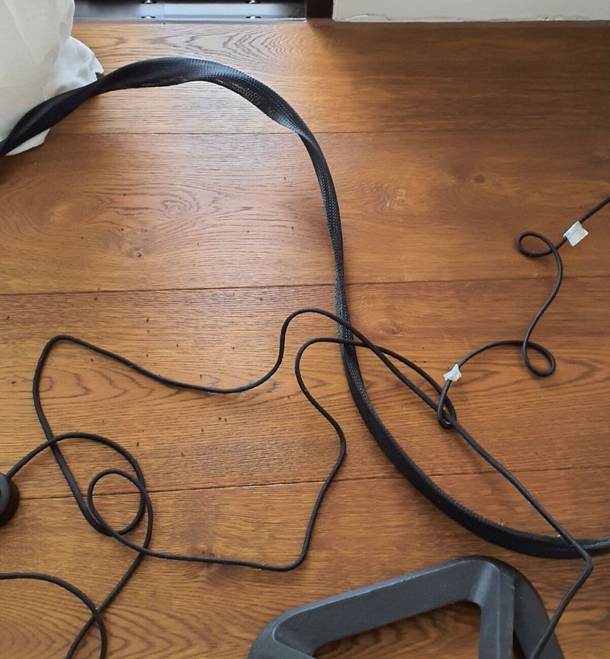  Auf einem Holzboden in Dänikon (8114, Kanton Zürich) liegen mehrere schwarze Kabel und ein Gerätekabelschutz lose verteilt neben einer Wand mit Sockelleiste.