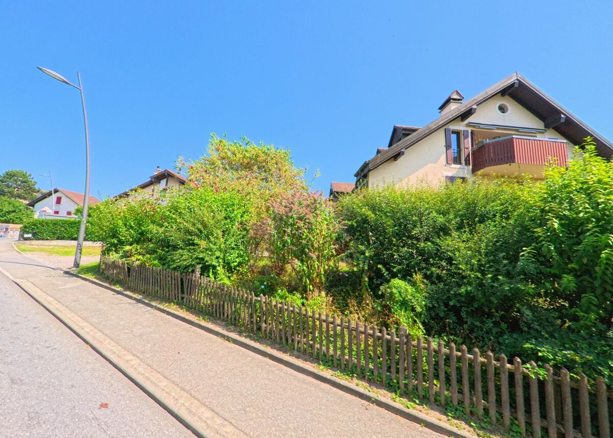 Entlang einer ruhigen Strasse in Daillens (1306, Kanton Waadt) stehen Haeuser mit Balkonen, die hinter dichten Straeuchern verborgen sind.