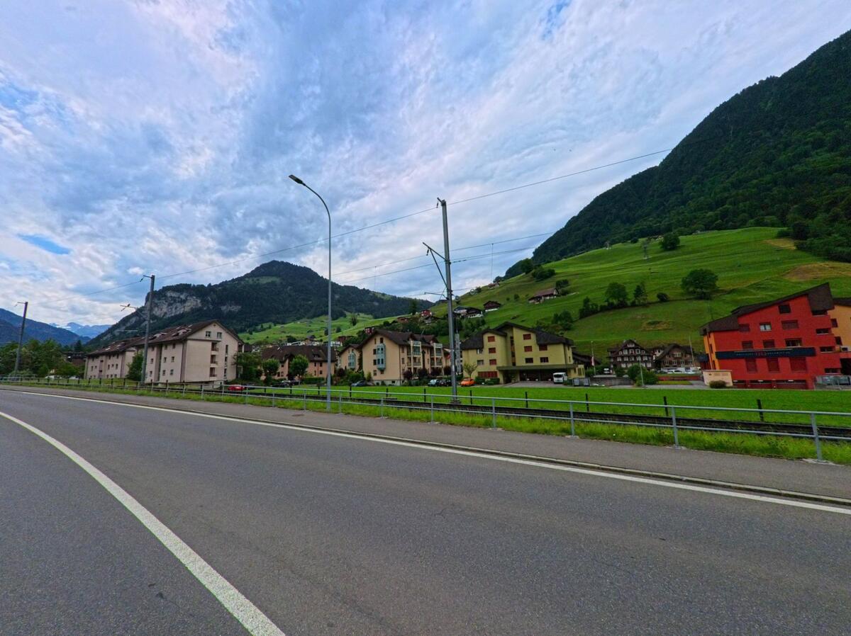 Zwischen Bahnlinie und Hauptstrasse erstreckt sich in Dallenwil (6382, Kanton Nidwalden) eine dichte Wohnsiedlung vor den steilen, grünen Haengen der umliegenden Berge.