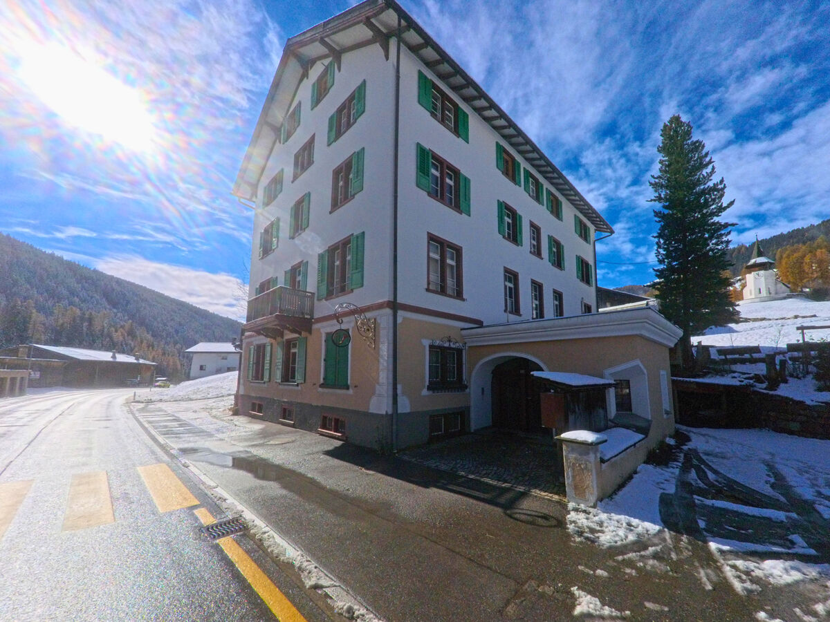 Ein Wohnhaus mit gruener Fensterlaeden steht an einer schmalen Ortsstrasse in Davos (7494, Kanton Graubünden).
