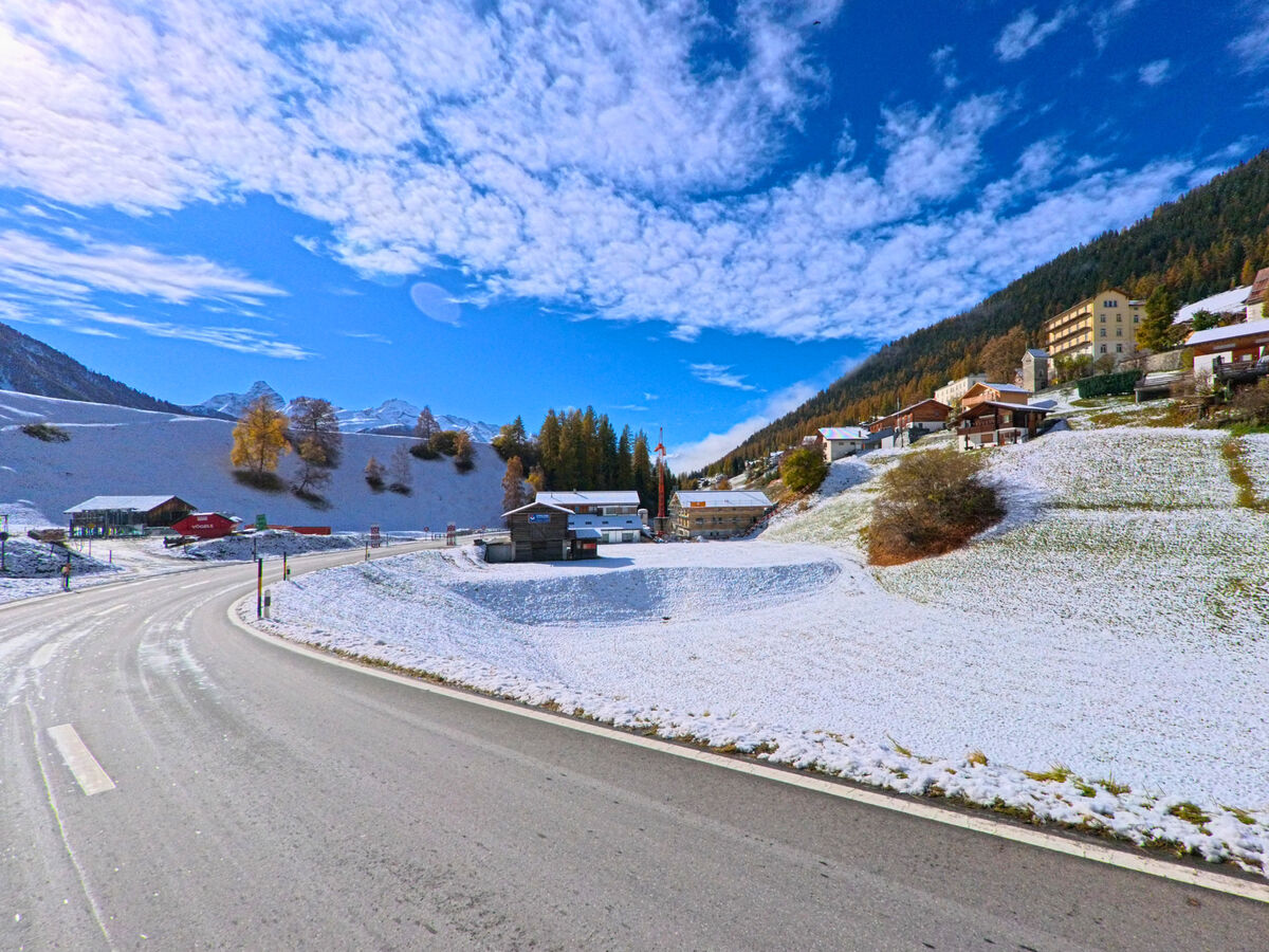 Eine Talstrasse verlaeuft in sanfter Kurve durch die verschneite Landschaft von Davos (7494, Kanton Graubünden).