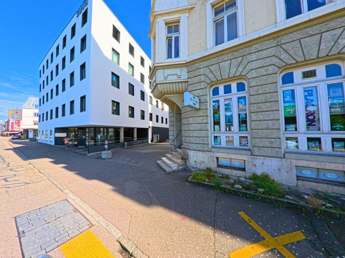 In Delémont (2800, Kanton Jura) treffen ein historisches Eckgebäude mit Stuckfassade und ein moderner Baukörper mit klaren Linien an einer Seitenstrasse aufeinander.