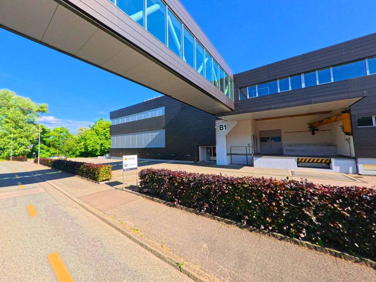 In einem Gewerbegebiet von Delémont (2800, Kanton Jura) verbindet ein verglaster Steg zwei moderne Industriegebäude über einer Anlieferungszone.