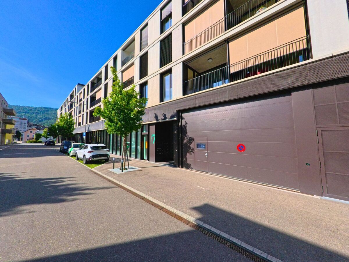 In einem modernen Quartier von Delémont (2800, Kanton Jura) reihen sich Neubauten mit Balkonen entlang einer schmalen Wohnstrasse mit parkenden Autos.