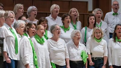 In Stein am Rhein (8260, Kanton Schaffhausen) singt ein gemischter Chor in weissen Oberteilen mit gruene Akzenten gemeinsam waehrend eines Auftritts im Innenraum.