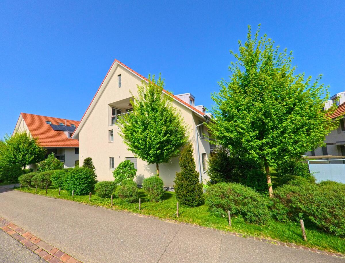 In Diegten (4457, Kanton Baselland) stehen moderne Mehrfamilienhaeuser mit hellen Fassaden und roten Daechern, umgeben von gepflegter Bepflanzung und jungen Baeumen.
