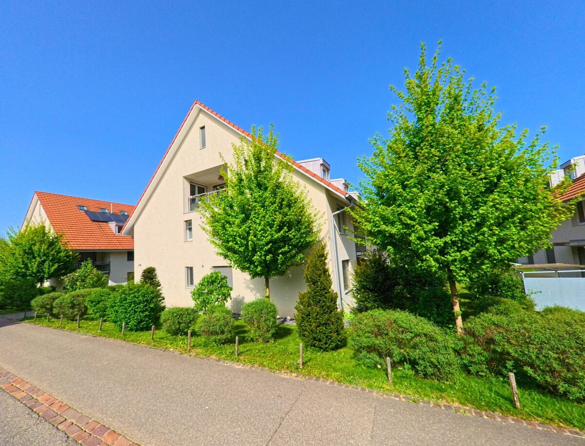 In Diegten (4457, Kanton Baselland) stehen moderne Mehrfamilienhaeuser mit hellen Fassaden und roten Daechern, umgeben von gepflegter Bepflanzung und jungen Baeumen.