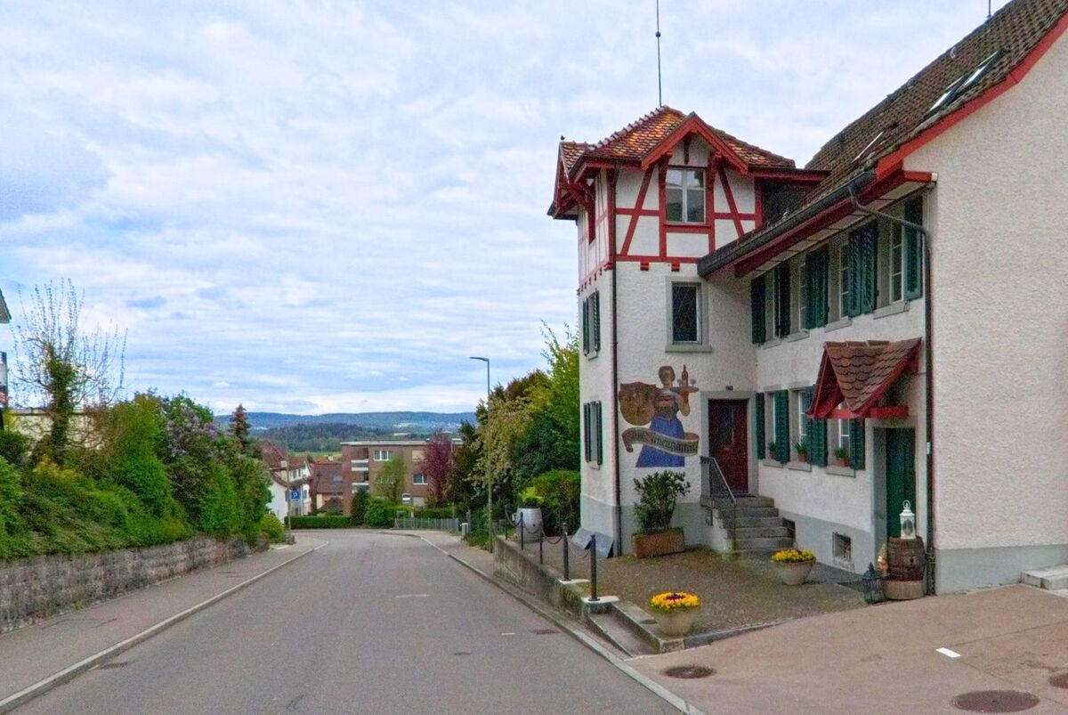In Dielsdorf im Kanton Zürich, PLZ 8157, steht an einer abfallenden Strasse ein historisches Gebäude mit Wandmalerei und Fachwerkelementen.