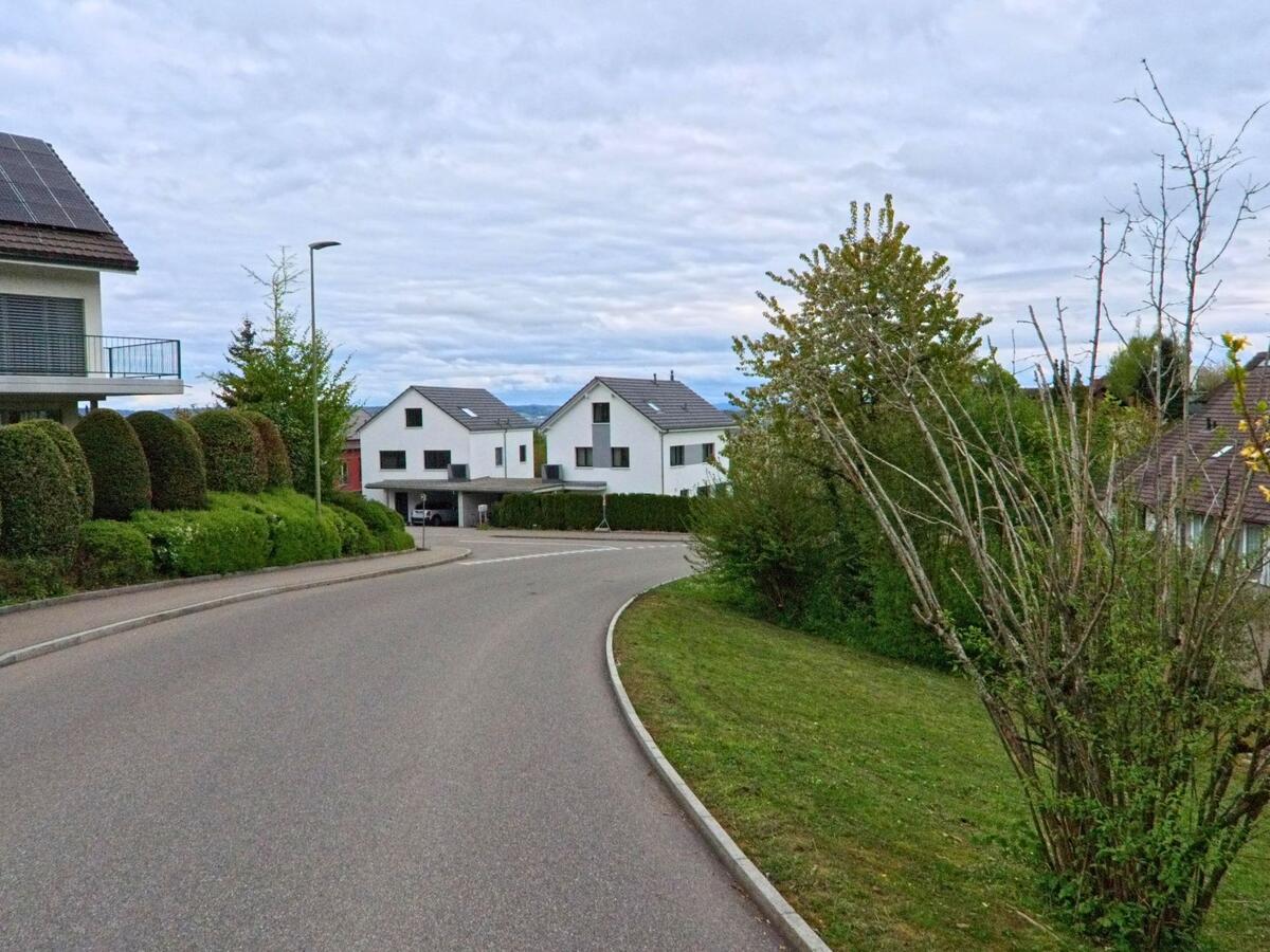 In einem Wohnquartier von Dielsdorf, PLZ 8157 im Kanton Zürich, säumt moderne Architektur mit weissen Einfamilienhäusern eine geschwungene Strasse.