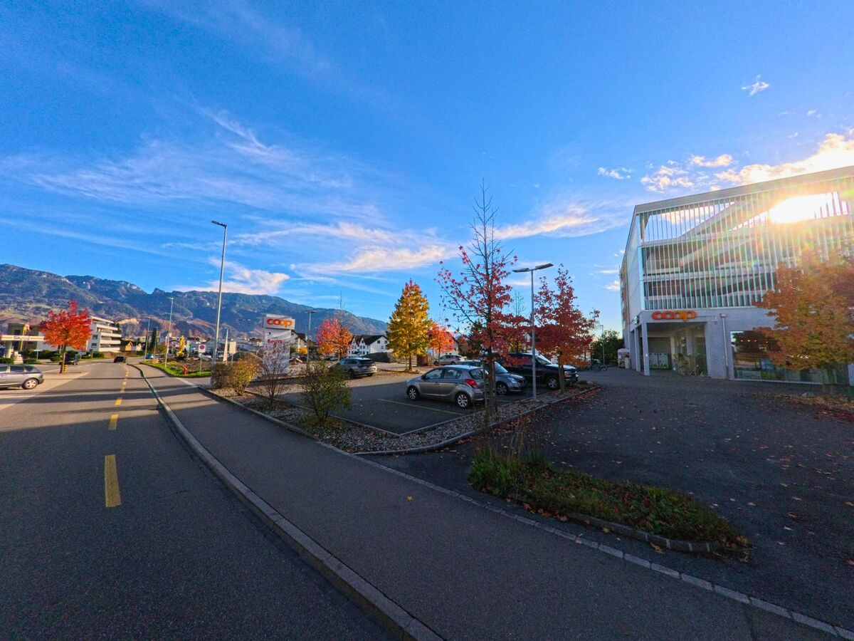 In Diepoldsau (9444, Kanton St. Gallen) verlaeuft eine ruhige Strasse entlang herbstlicher Baeume, waehrend rechts ein Coop-Parkplatz vor Bergkulisse liegt.