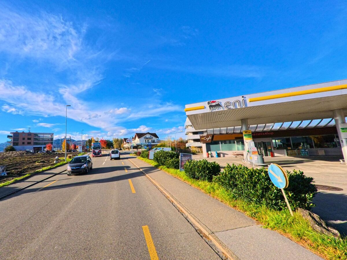 Auf einer belebten Strasse in Diepoldsau (9444, Kanton St. Gallen) passiert der Verkehr eine Tankstelle, waehrend moderne und traditionelle Gebaeude die Szene praegen.