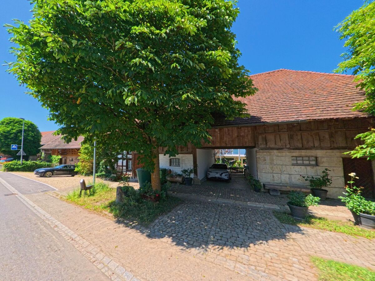 In Diessbach bei Büren (3264, Kanton Bern) steht ein traditioneller Bauernhof mit breitem Durchgang und gepflastertem Vorplatz im Schatten großer Bäume.