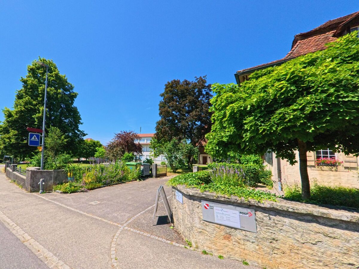 In Diessbach bei Büren (3264, Kanton Bern) liegt ein gepflegter Garten mit Verwaltungsgebäude neben einem Fußgängerübergang und einer Schulwegmarkierung.
