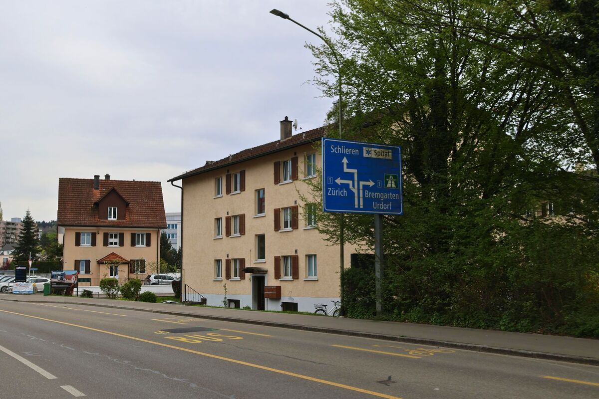 In Dietikon (8953, Kanton Zürich) saeumen schlichte Wohnhaeuser die Strasse, waehrend ein blaues Wegweiser­schild Richtung Schlieren, Zürich und Bremgarten fuehrt.