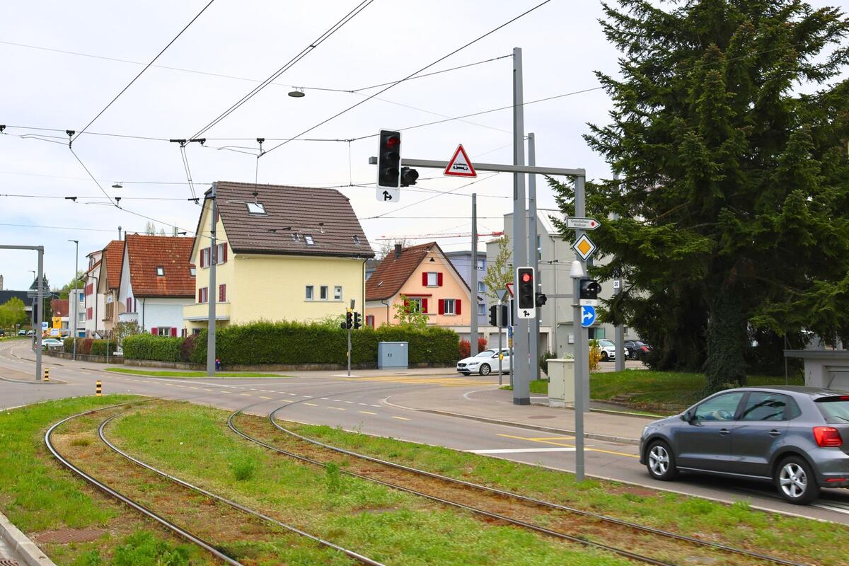 In Dietikon, PLZ 8953 im Kanton Zürich, verläuft eine Strassenbahnkurve durch ein Wohnquartier mit Ampelanlagen und farbigen Einfamilienhäusern.