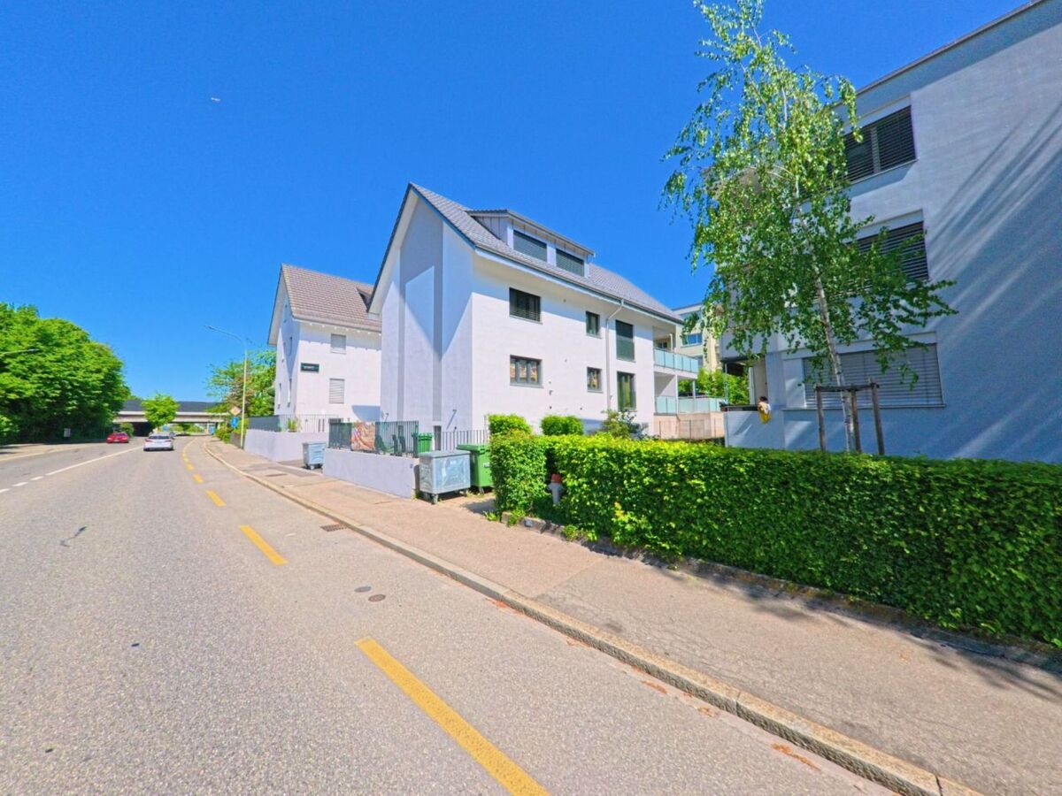 In Dietikon im Kanton Zürich, PLZ 8953, säumen moderne weisse Wohnhäuser eine sonnige Strasse mit Radweg in unmittelbarer Nähe zur Autobahn.