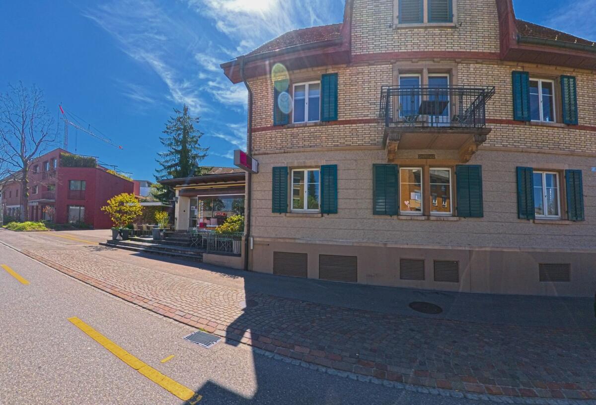 In Dietlikon, PLZ 8305 im Kanton Zürich, steht an einer gepflasterten Strasse ein historisches Wohn- und Geschäftshaus mit grünen Fensterläden und kleinem Ladeneingang.