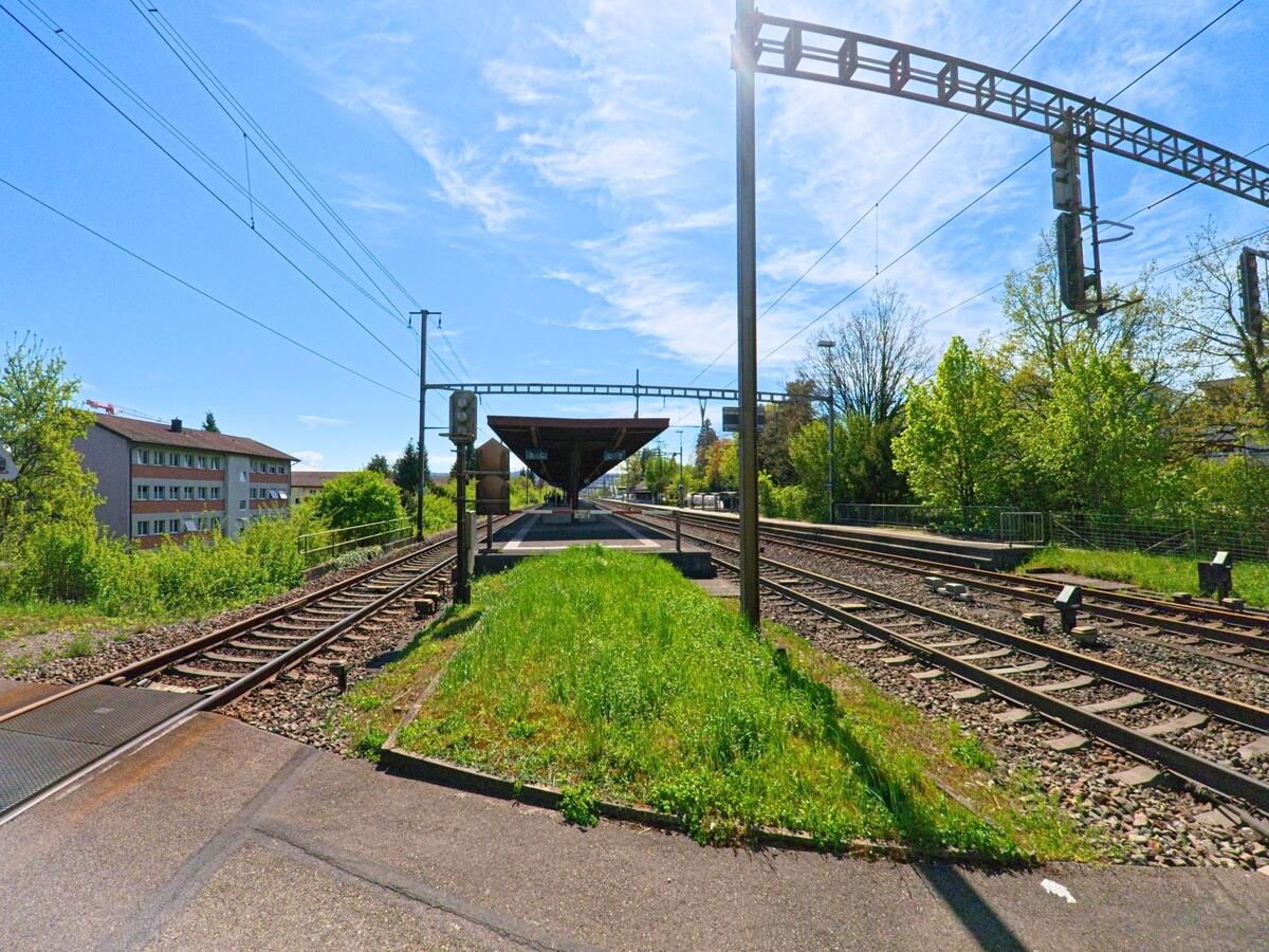 In Dietlikon, PLZ 8305 im Kanton Zürich, liegt der Bahnhof mit überdachten Bahnsteigen zwischen mehreren Gleisen und angrenzender Wohnbebauung.