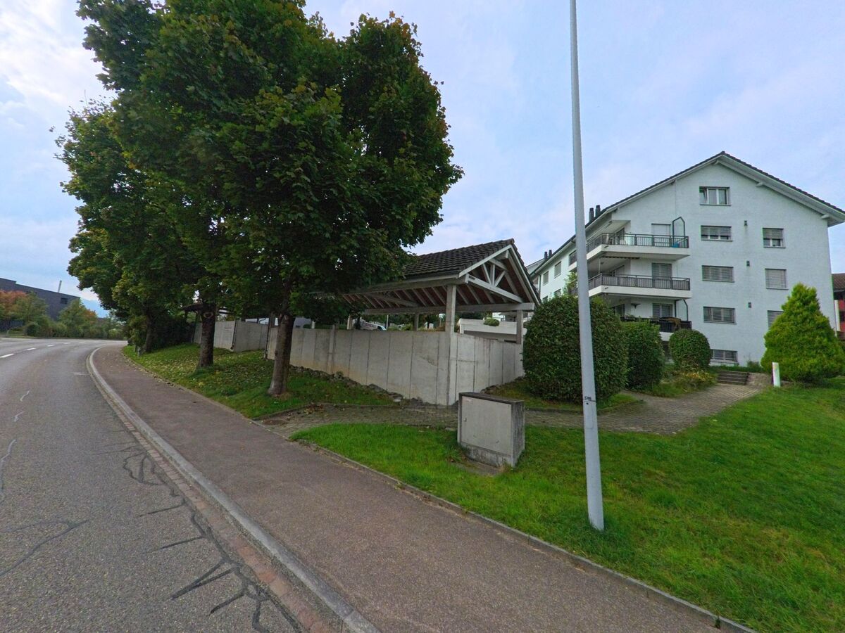Entlang der Hauptstrasse in Dietwil (6042, Kanton Aargau) stehen Mehrfamilienhäuser mit Balkonen und gepflegten Grünflächen unter schattigen Bäumen.