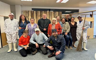 Eine Gruppe des Dorftheaters Widnau posiert in Kostümen vor einer Holzwand in einem Innenraum in Widnau, 9443, Kanton St. Gallen.