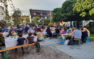 Auf dem Dorfplatz in Nussbaumen (8537, Kanton Thurgau) sitzen zahlreiche Familien an langen Tischen im Freien und geniessen gemeinsam ein Fest.