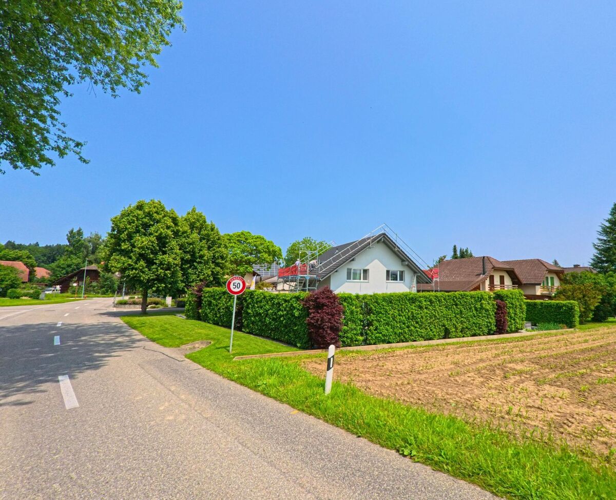 In Drei Höfe (4558, Kanton Solothurn) markiert ein 50er-Tempolimit die Einfahrt in ein Wohnquartier mit Einfamilienhäusern und gepflegten Hecken entlang eines Feldrands.