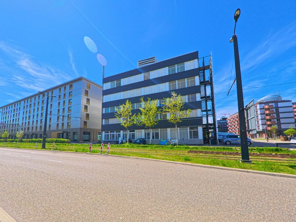 In [ORT], PLZ [PLZ], im [KANTON] reihen sich moderne Büro- und Wohngebäude entlang einer breiten Strasse mit Tramgleisen unter blauem Himmel aneinander.