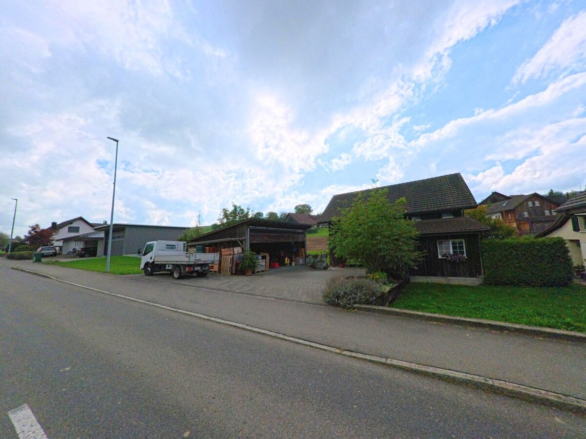 Ein Bauernhof mit offener Scheune und geparktem Lieferwagen liegt an einer Nebenstrasse in Dürrenäsch (5724, Kanton Aargau), im Hintergrund sind weitere Wohnhäuser zu sehen.