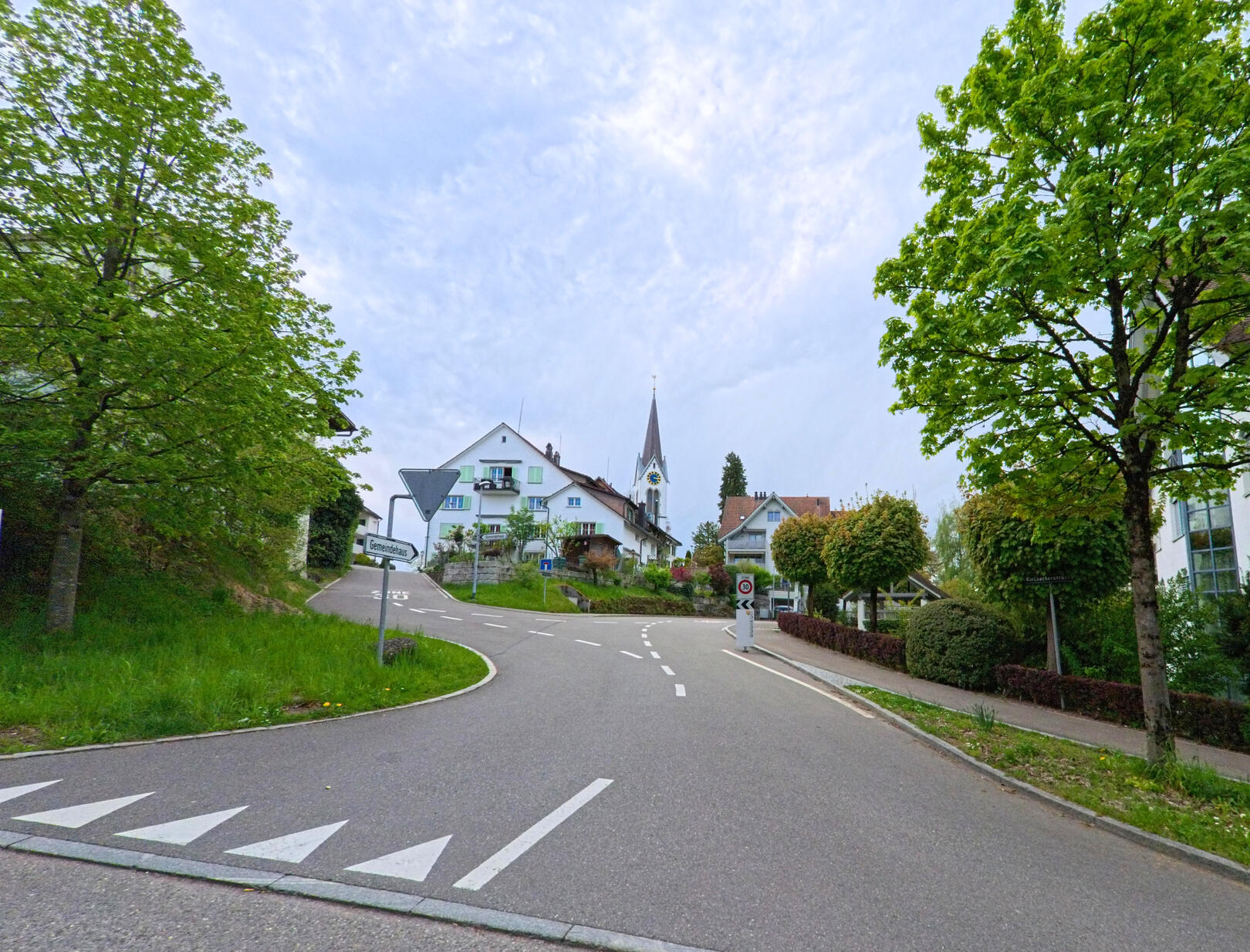 In Dürnten (8608, Kanton Zürich) steigt eine Strasse sanft an, gesäumt von Bäumen, und führt vorbei an Wohnhäusern mit Blick auf den Kirchturm.