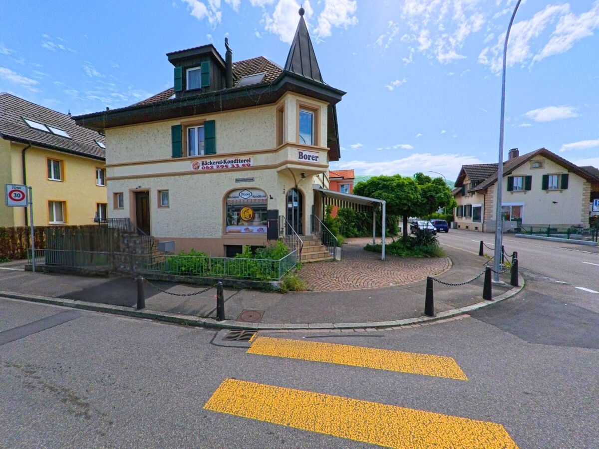  In Dulliken (4657, Kanton Solothurn) befindet sich eine Bäckerei-Konditorei im Erdgeschoss eines Hauses mit markantem Türmchen an einer verkehrsberuhigten Strassenecke.