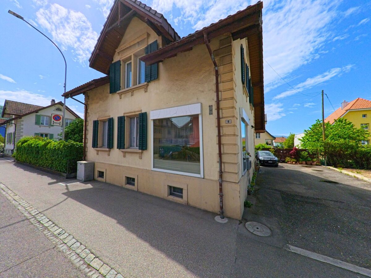 In Dulliken (4657, Kanton Solothurn) steht ein älteres Einfamilienhaus mit grünen Fensterläden und grossem Schaufenster an einer ruhigen Quartierstrasse.
