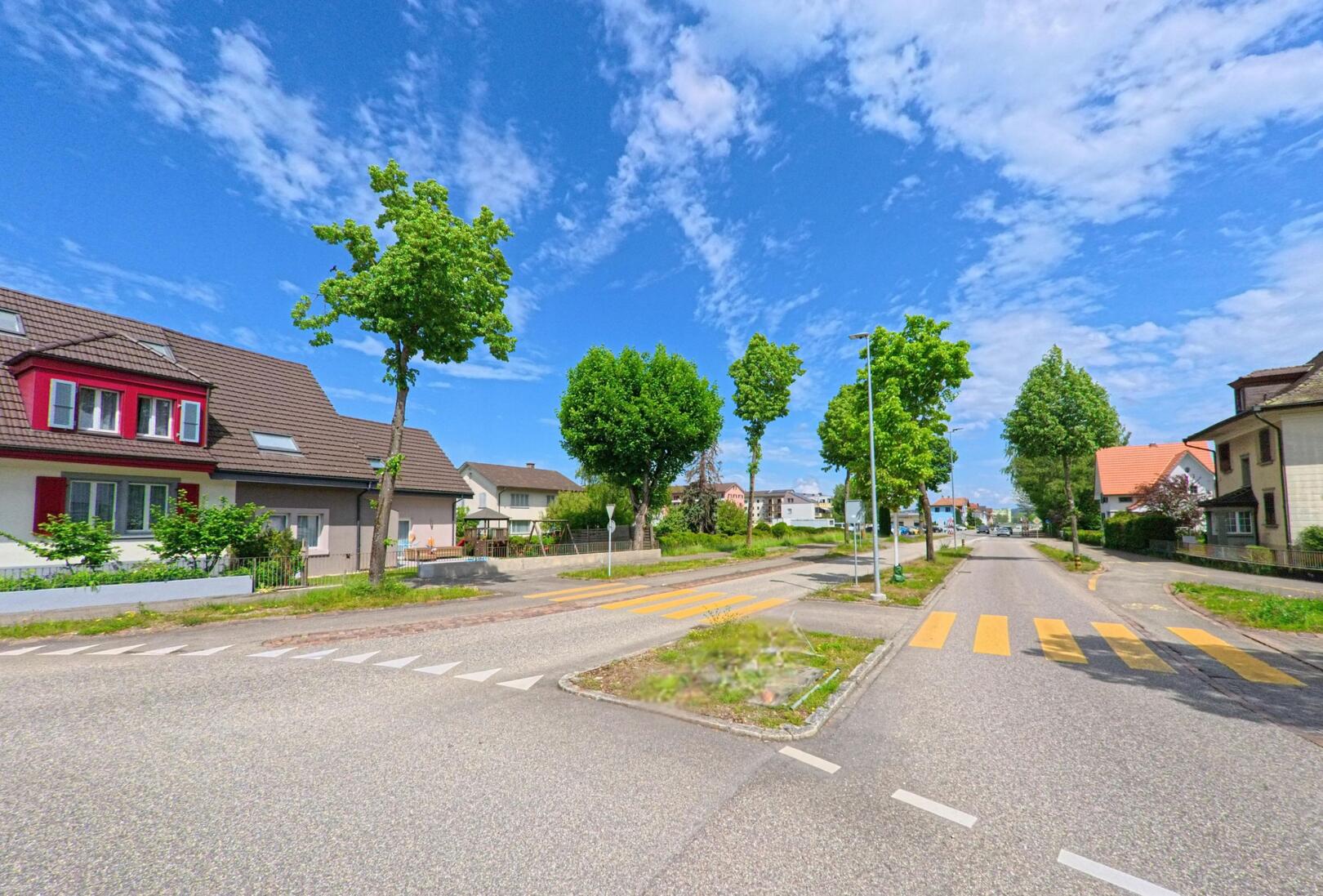 In Dulliken (4657, Kanton Solothurn) verläuft eine verkehrsberuhigte Strasse mit Zebrastreifen und Mittelinsel durch ein Wohnquartier mit Einfamilienhäusern und Bäumen.