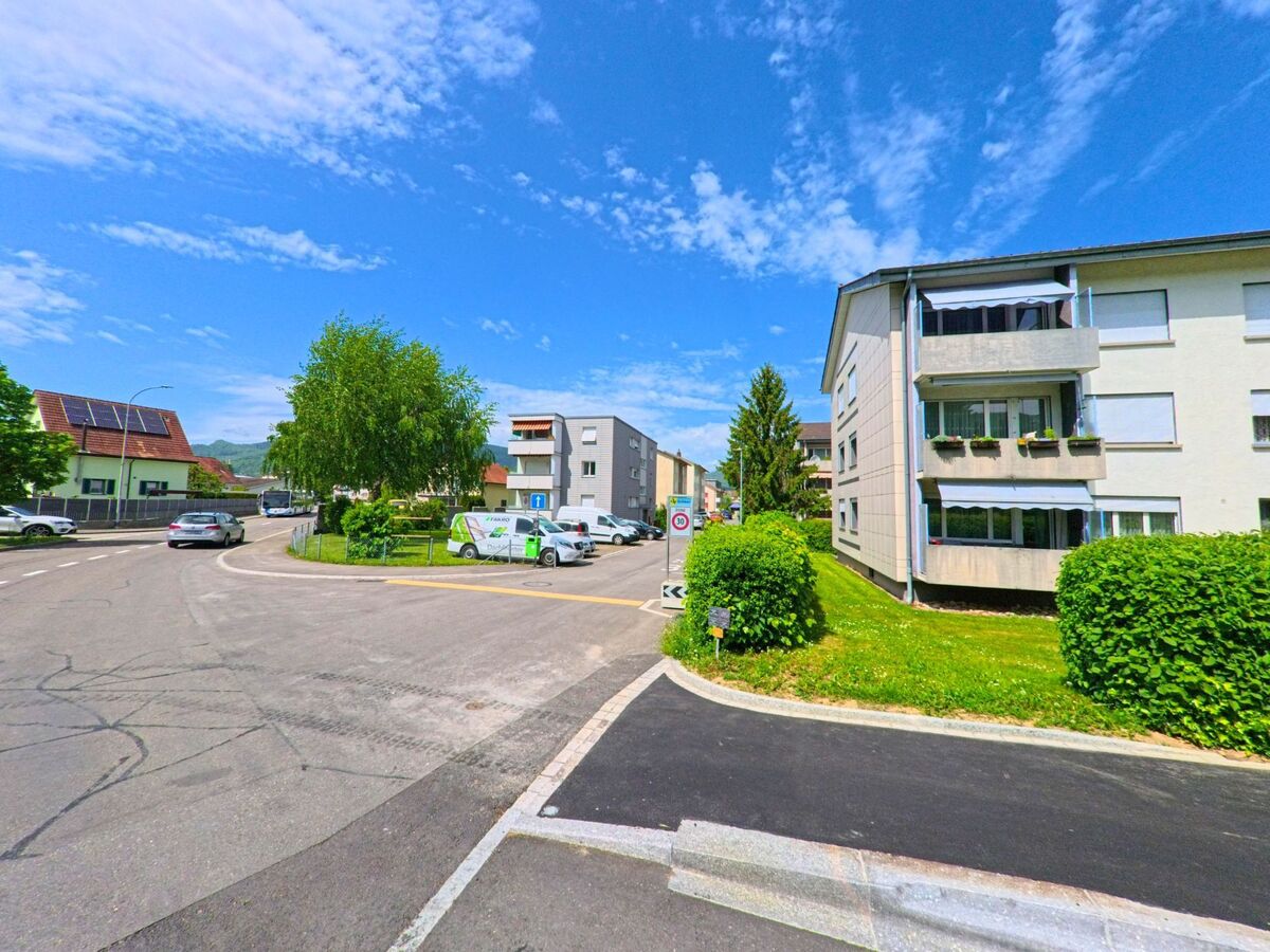 In Dulliken (4657, Kanton Solothurn) zeigt sich ein ruhiges Wohnviertel mit Mehrfamilienhäusern, gepflegten Grünflächen und parkenden Fahrzeugen an einer Einmündung.