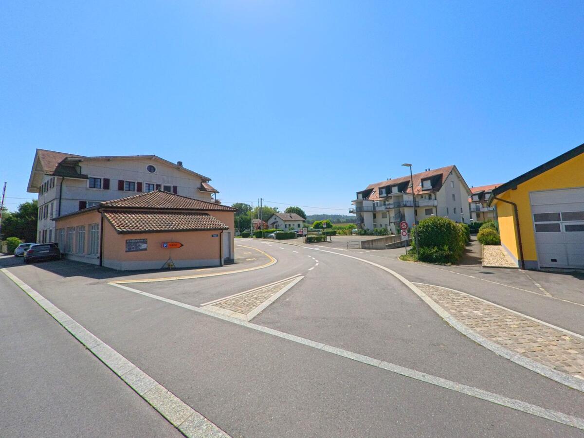 Am Ortsrand von Echallens (1040, Kanton Waadt) fuehrt eine Strasse an Wohnhaeusern und Gewerbegebaeuden vorbei in Richtung offenes Land.