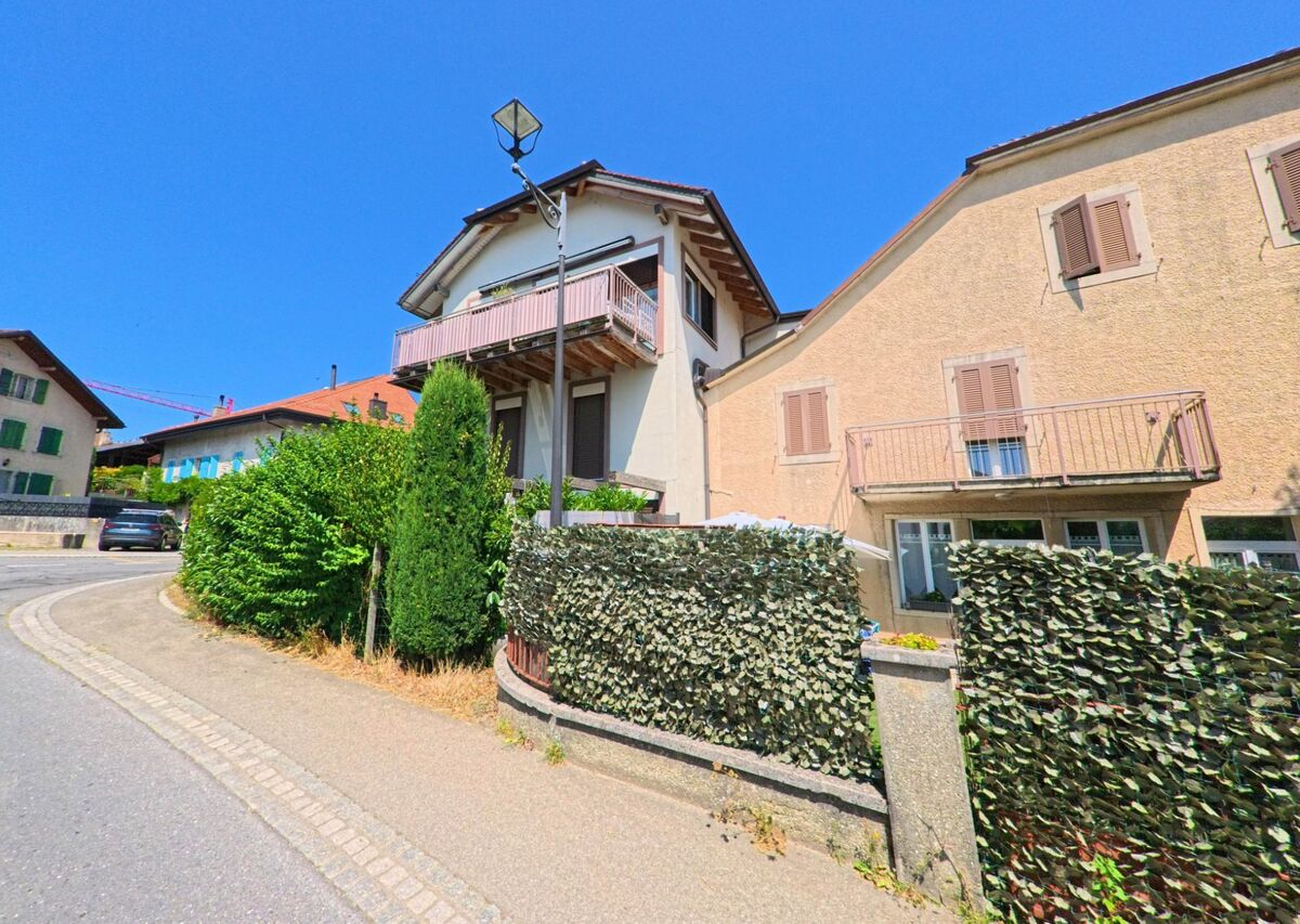 Wohnhaeuser mit Balkonen und Fensterlaeden stehen an einer leicht gekruemmten Strasse in Echichens (1112, Kanton Waadt).