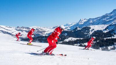 In Villars s/Ollon (1884, Kanton Waadt) fahren Skilehrer der Ecole Suisse de Ski et de Snowboard in roter Uniform uebers weisse Schneefeld vor imposanter Bergkulisse.