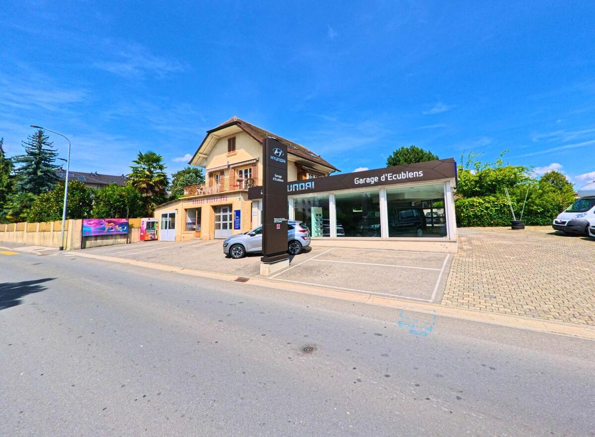 In Ecublens (1024, Kanton Waadt) befindet sich eine Autogarage mit Glasfassade und einem angrenzenden Wohnhaus an einer Nebenstrasse.