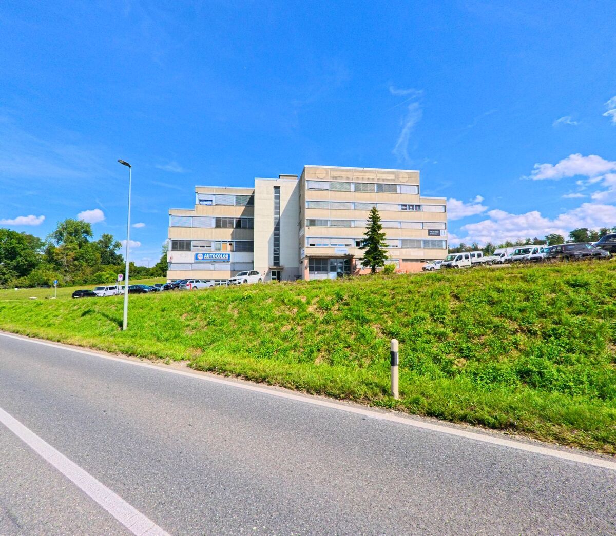 Ein mehrstöckiges Bürogebäude in Ecublens (1024, Kanton Waadt) steht oberhalb einer Gruenflaeche an einer Hauptstrasse.