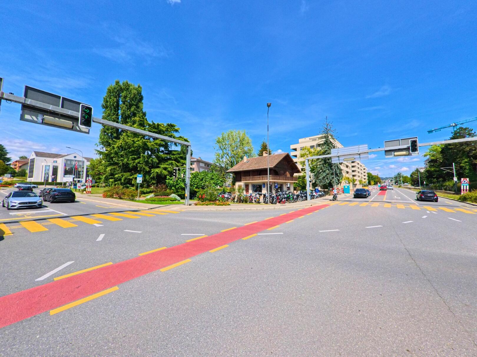 An einer grossen Kreuzung in Ecublens (1024, Kanton Waadt) stehen ein kleines Holzhaus und moderne Wohnbauten neben der Strasse.