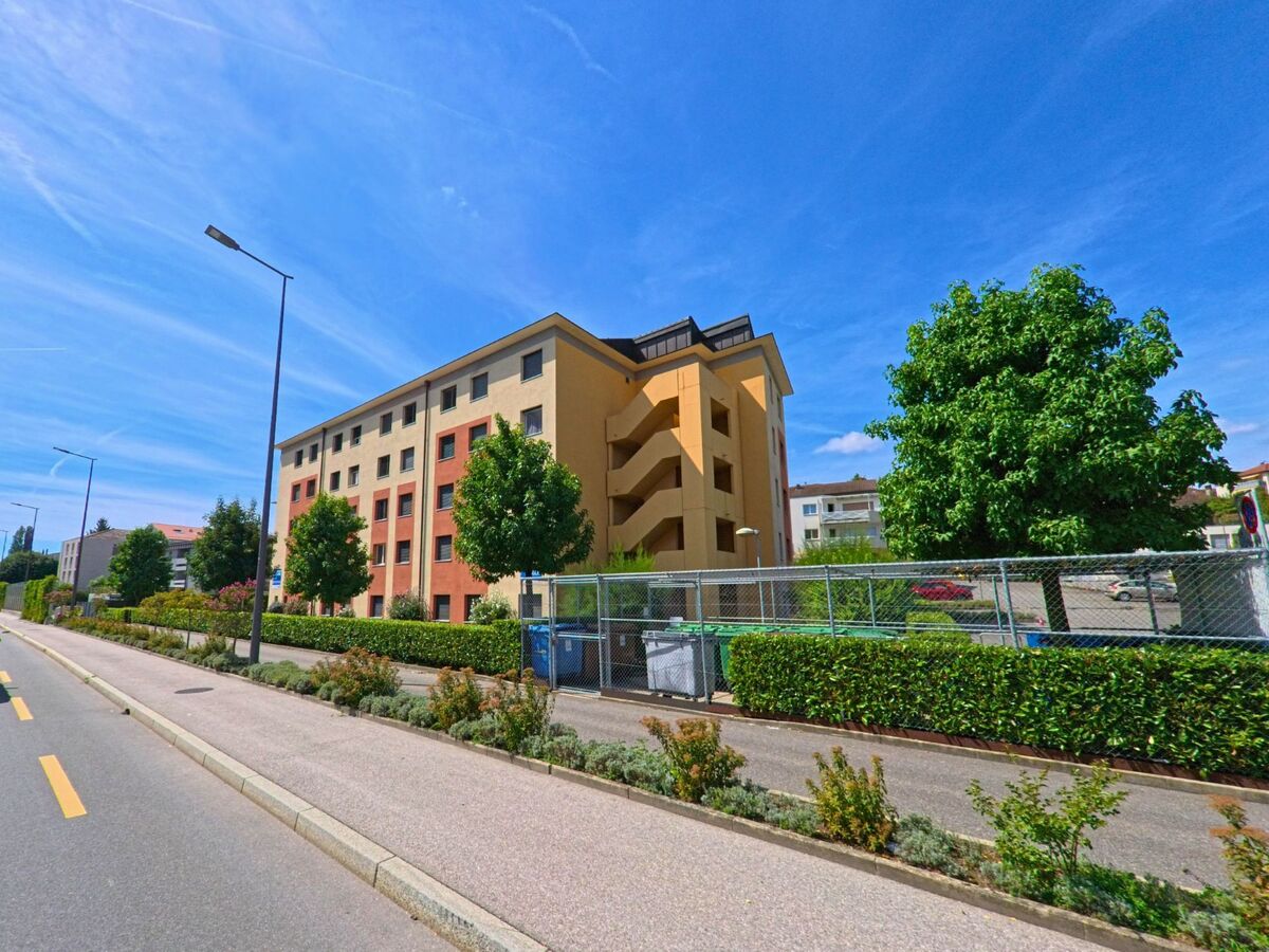 In Ecublens (1024, Kanton Waadt) steht ein Wohnhaus mit farbigen Fassaden und begruentem Vorbereich an einer Nebenstrasse.