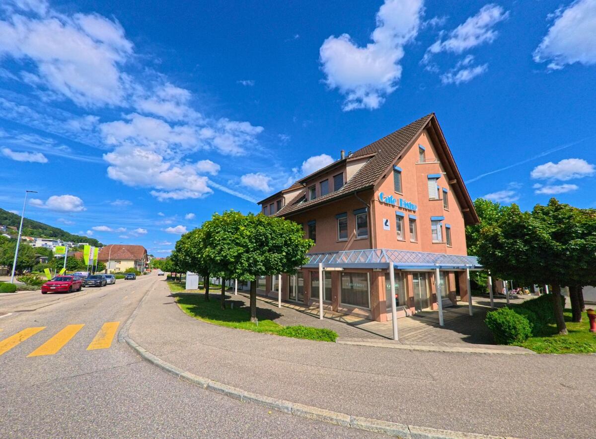 Das markante Gebäude mit dem Schriftzug Café Bistro steht an einer Kreuzung in Egerkingen (4622, Kanton Solothurn) und ist von Bäumen sowie breiten Gehwegen umgeben.