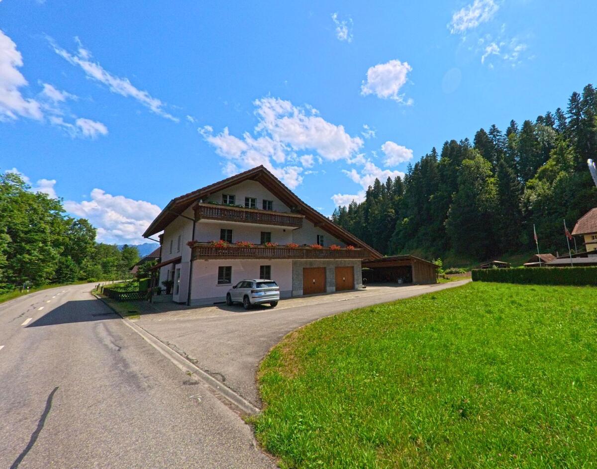 Ein Wohnhaus mit Blumenbalkonen steht in Eggiwil (3536, Kanton Bern) direkt an einer kurvigen Landstrasse, begrenzt von Wiesen und einem bewaldeten Hang.