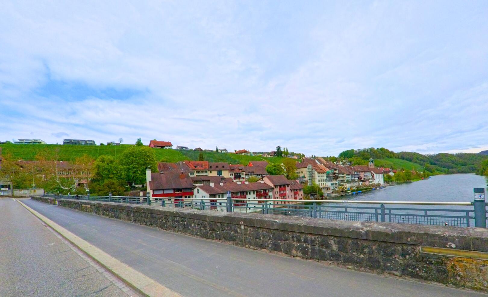 Von der Rheinbrücke in Eglisau, PLZ 8193 im Kanton Zürich, blickt man auf die farbigen Häuser entlang des Ufers und die dahinterliegenden Rebberge.