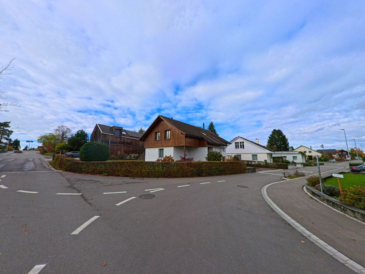 Eine ruhige Kreuzung in Egnach (9322, Kanton Thurgau) führt an Einfamilienhäusern und Hecken vorbei, während sich der Himmel weit über dem Quartier öffnet.