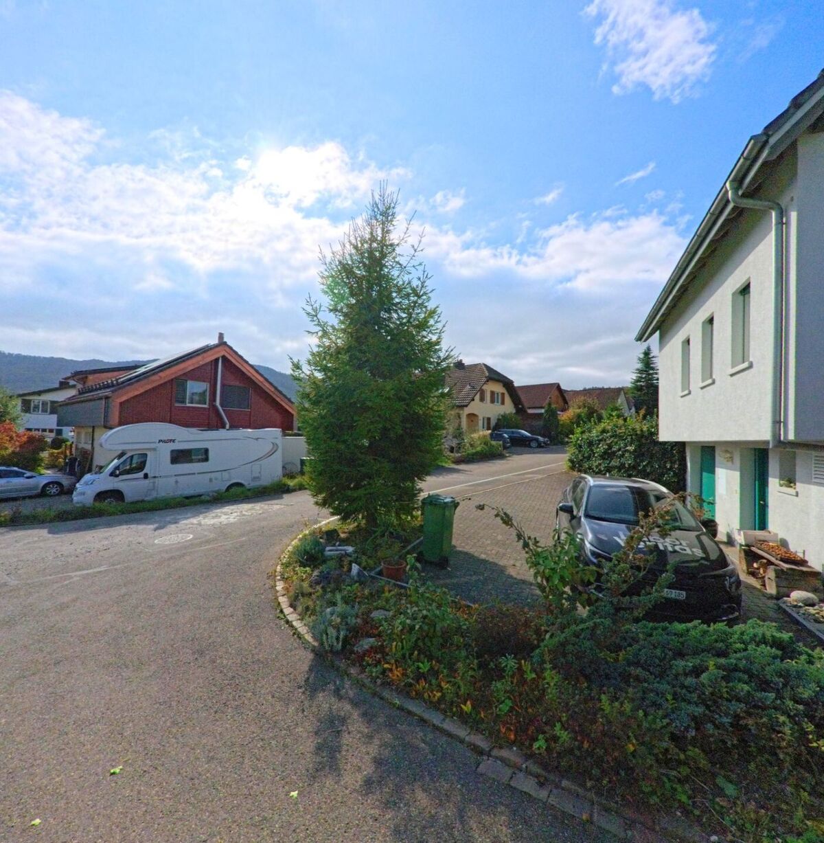 In einem Wohnquartier von Ehrendingen (5420, Kanton Aargau) stehen Einfamilienhäuser mit gepflegten Gärten, einem Wohnmobil und parkenden Autos unter blauem Himmel.