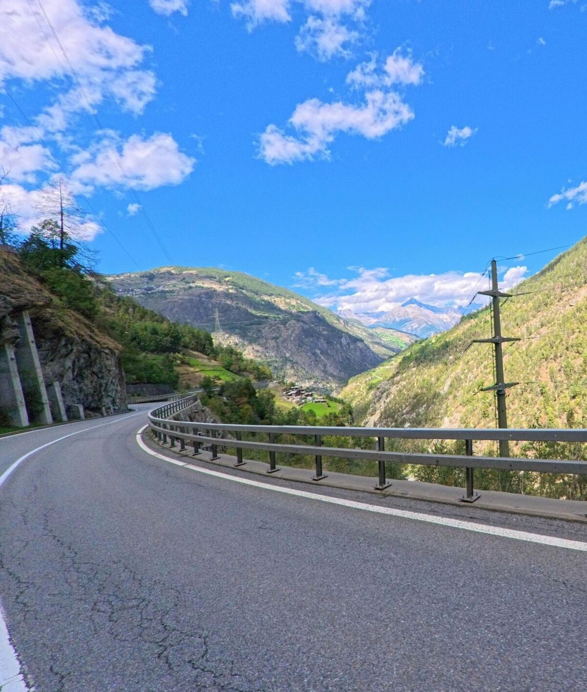 Eine kurvenreiche Bergstrasse in Eisten (3922, Kanton Wallis) führt entlang steiler Hänge mit weitem Blick ins alpine Tal unter blauem Himmel.