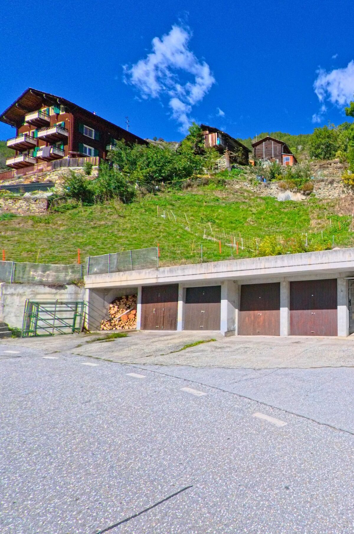 Mehrere Holzhäuser stehen am Hang in Embd (3926, Kanton Wallis), darunter befinden sich Garagen mit geschlossenen Toren und einem Stapel Holz.